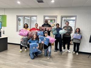 Several people from Onward Injury Law and Western Avenue Community Center are holding up coats that were donated to families in the Bloomington, IL community.