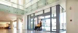 A lady pushing a man in his wheel chair through an automatic door 