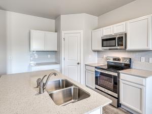 Kitchen featuring stainless steel appliances, decorative backsplash, an island with sink, white cabinetry, and walkin pantry