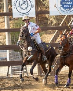 an arena polo player hits a ball under his horse's neck