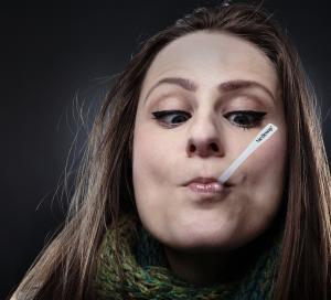 Woman using a disposable NexTemp Go thermometer to take her temperature orally. She is looking down at the thermometer and reading her temperature while the thermometer is in her mouth