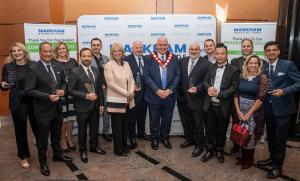 A group photo at the 2024 Business Excellence Awards featuring the award recipients holding their trophies, along with Mayor Frank Scarpitti standing in the middle wearing the ceremonial chain of office. The backdrop displays Markham Board of Trade banner