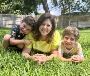 Shaina Williams, a licensed therapist, lies in the grass smiling with her two young children, who inspired her coloring book Color Your Feelings, which promotes emotional awareness and creativity.