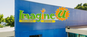 Imagine U Children's Museum sign on a blue building facade under a clear sky.