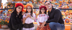 Family in traditional Mexican attire at a colorful Day of the Dead altar.