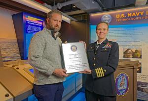 Navy CAPT Jessica O'Brien, Commanding Officer, Naval Weapons Station Seal Beach, presents the Secretary of the Navy 2024 Environmental Award to Jonathan Williams, President and CEO of Pacific Battleship Center.