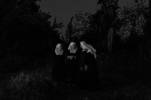 four sisters standing in the darkness, talking, with a feint bit of moonlight and trees in the backdrop