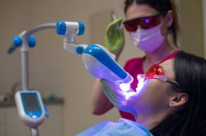  Female patient undergoing professional teeth whitening with a light-activated dental instrument.