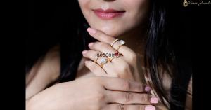 A woman's hand wearing multiple gold rings featuring a lab-grown diamond, a lab-grown ruby, and a moissanite gemstone.