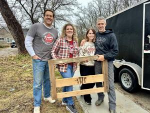 A group of four volunteers hold a wooden SHP headboard outside.