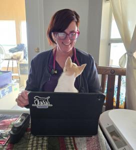 Dr. Rusch in a house call visit with an inquisitive patient, a cat named Ty sitting on her laptop.