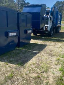 A truck places a dumpster alongside two other blue dumpsters arranged for waste collection or disposal in a neat, organized setting.