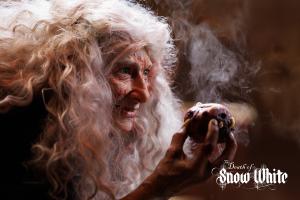 The evil witch holds a rotting apple with a menacing look on her face and smoke in the background from a scene in the movie, the Death of Snow White