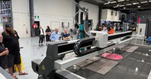 A waterjet cutting machine operating in a spacious workshop, with onlookers gathered around to observe the industrial tools and machines at work.