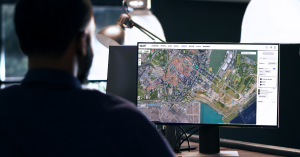 A person sits at a desk viewing Quori's mapping feature on a computer screen, displaying a satellite image with security monitoring overlays.