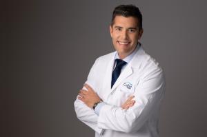 Dr. O’Neill, a Board-Certified Ophthalmologist with advanced subspecialty training in cataract and refractive surgery, smiling and wearing a professional white coat in a medical office setting.