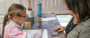 A child and adult sitting at a table with educational materials.