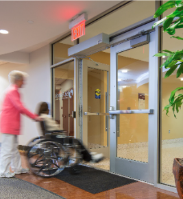 Woman pushing a wheelchair smoothly through an automatic door, demonstrating accessibility and convenience.