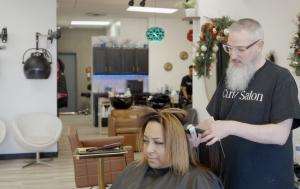 A man with a beard expertly straightens a woman's hair in a modern salon environment.