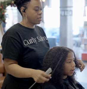 A woman stylist carefully creates a fresh and stylish look for the child.