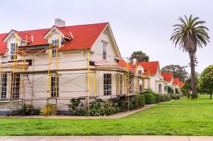 Street view of a row of identical houses, with the first house undergoing exterior renovations, including new siding and fresh paint.