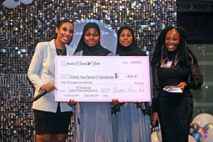 Jasmine LeFlore and Dr. Brittany Wheeler of Greater Than Tech (GTT), stand smiling while presenting a large ceremonial check for $1,000 to two young women, Hawaa Bahreldin and Fatima Bahreldin during a GTT event. Both recipients are wearing black hijabs. 