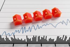 Row of red toy houses on a fluctuating line graph with transaction volumes indicated as bar chart at the bottom