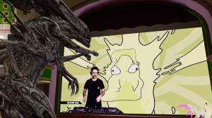 A dramatic scene featuring a DJ performing at a mixing console against a yellow background with an abstract cartoon face design. The striking focal point is a large, menacing xenomorph-style alien sculpture looming over the DJ setup from the left side, cr