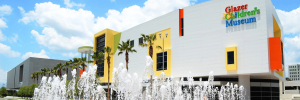 Exterior of Glazer Children's Museum with fountain in front, under a clear sky.