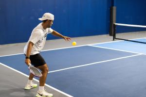 Man playing pickleball on and indoor court about to serve.