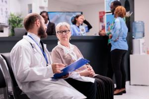 A physician discusses health concerns with a senior woman while medical staff at the reception desk assist a couple with their healthcare inquiries, ensuring seamless access to medical services.