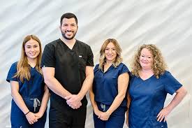 Dr. Aryan Abedini and the Love Dental staff, wearing navy scrubs, smiling as they stand together in front of a neutral backdrop, representing their commitment to quality dental care.