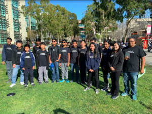 A team of 13 middle school students in matching shirts pose with their coach holding a plaque.