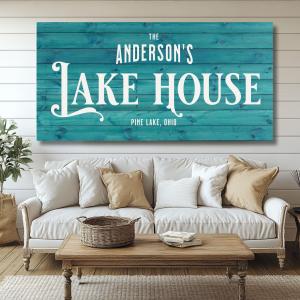 Photo shows a personalized family name sign above a couch.  The sign is aqua blue in color with white text showing the family's last name above the words Lake House.