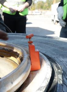 A closeup of a high-visibility orange 3-Step tool in the tire bead to keep tire techs' fingers safe. In the background of the photo, techs watch the demonstration.