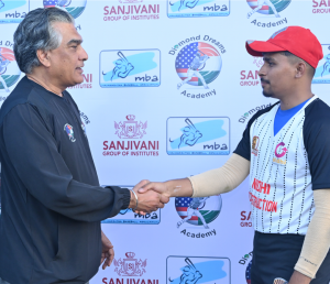 Two men shaking hands in front of a backdrop featuring logo of Diamond Dreams Academy. Kanwal Sra, CEO DDA is wearing a black DDA T-shirt, and the DDA Player is wearing a baseball cap and a sports jersey.