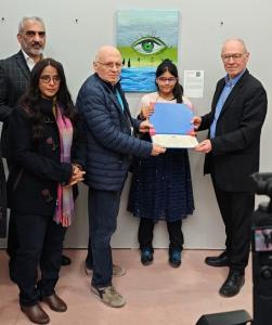 Aaradhya, an 11-year-old artist from Singapore, receives her Art Capital Paris 2025 certificate from Alain Bazard and Bruno Madelaine, standing in front of her artwork The Eye of Nature, displayed at Grand Palais Éphémère, Paris.