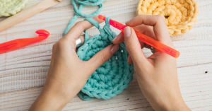 a person crocheting with a plastic crochet hook and thick blue yarn