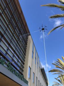 A drone spraying water on the windows of the Specialty Center at Torrance Memorial Medical Center (TMMC), showcasing SprayTech’s advanced drone-powered cleaning technology.