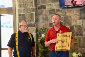 A man presents a wooden award plaque to another man