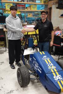 Two persons shaking hand standing next to UBC Formula Electric racing car