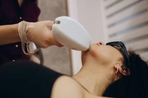 An aesthetician performs a laser hair removal treatment on a woman’s face.