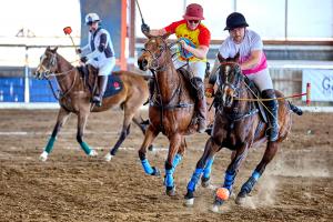 two polo players ride after a ball with umpire watching in the background