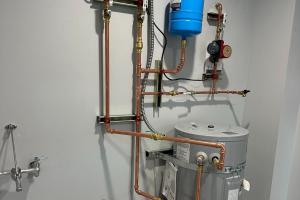 A professionally installed high-efficiency water heater system featuring copper piping, a blue expansion tank, and a circulation pump, mounted securely in a clean, modern utility space.