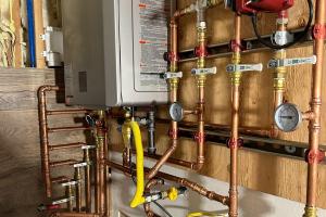 A state-of-the-art tankless water heater with precision copper piping, pressure gauges, and a yellow gas line, securely installed on a wooden wall for efficient hot water delivery.