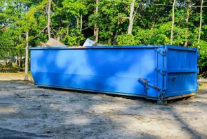 A large blue commercial dumpster in a backyard, ready for waste disposal and debris management.