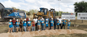 A diverse group of adults and children in hard hats poses with shovels at a groundbreaking event for Fritz Park Phase 2.