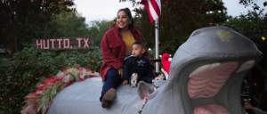 A woman and a child sit on a large, colorful hippopotamus sculpture, surrounded by festive lights and an American flag nearby.