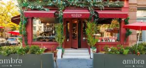 Exterior view of Ambra NYC, a charming Italian restaurant with a rustic red facade, lush greenery, and elegant outdoor seating.