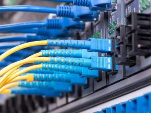 A close-up of blue and yellow fiber optic cables plugged into a network switch, showing the setup and organization of fiber optic cabling for high-speed data transmission.